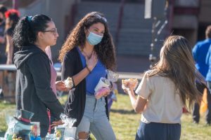 Three students with long hair hold snacks and talk