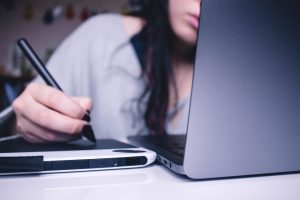 A person behind a laptop writing on a tablet.