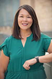 Dr. Rosemary J. Perez, a Filipina woman in a green dress, smiles at the camera while leaning her arm on a wall