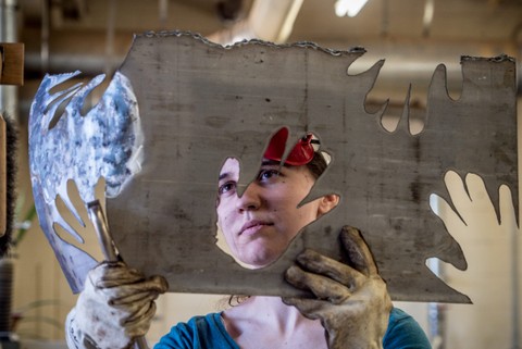Student working with a piece of metal for a sculpture